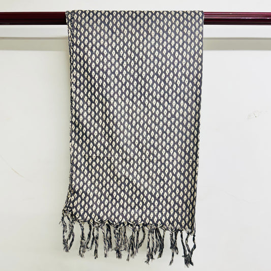 Black and white patterned scarf with fringes on a wooden rod against a white background