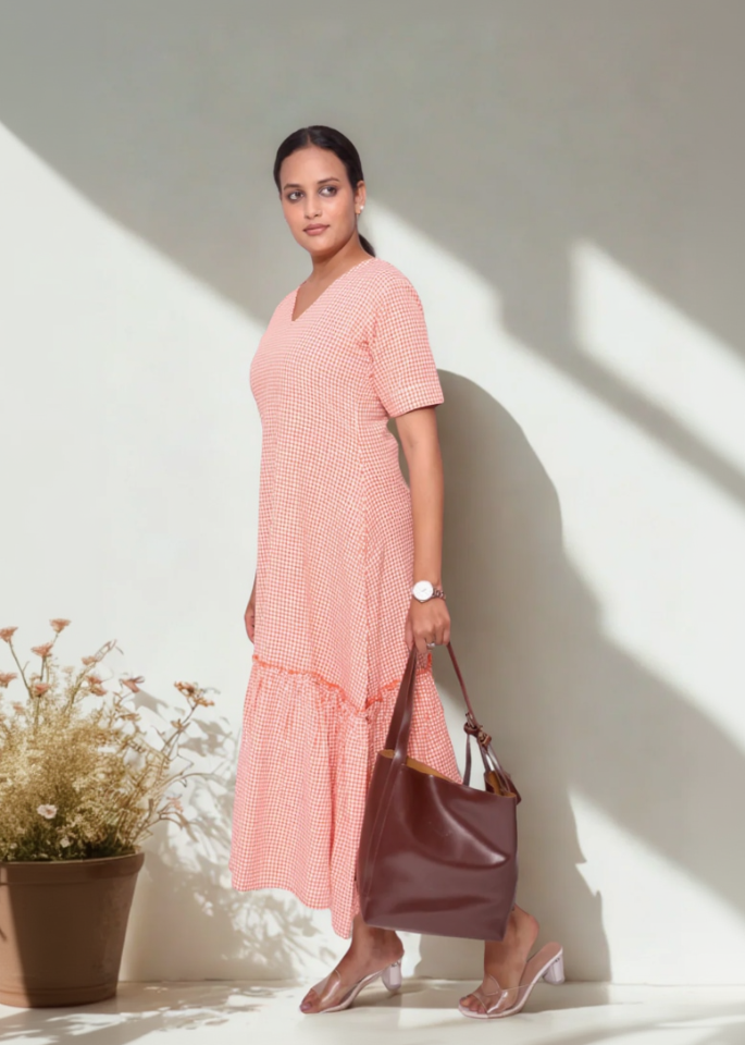 Woman in a pink dress holding a brown bag against a white wall.