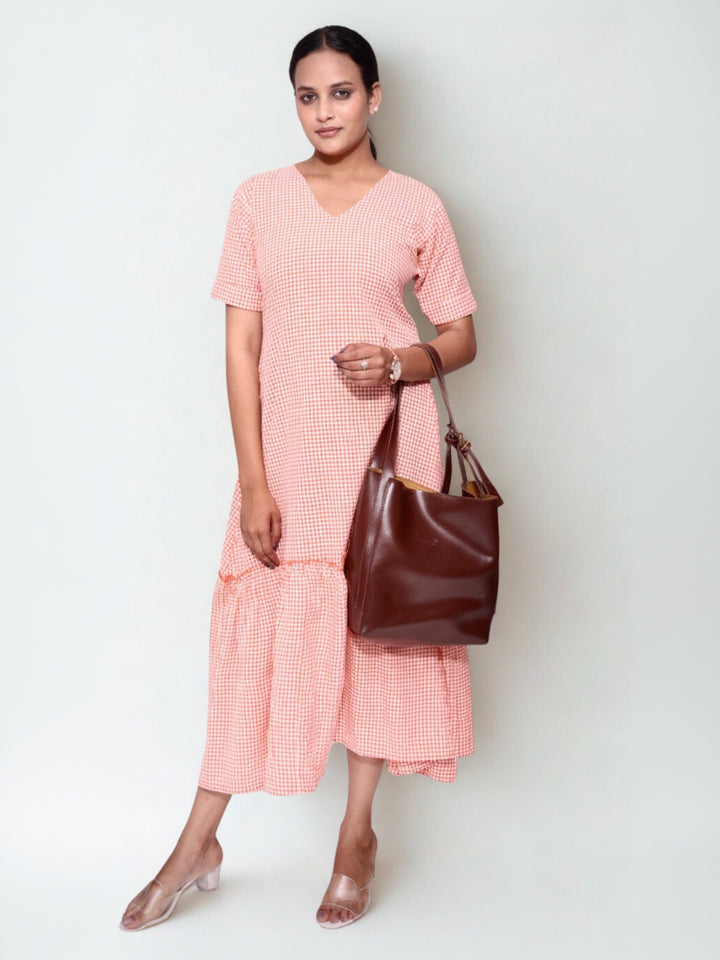 Woman wearing a pink dress holding a brown handbag against a white background